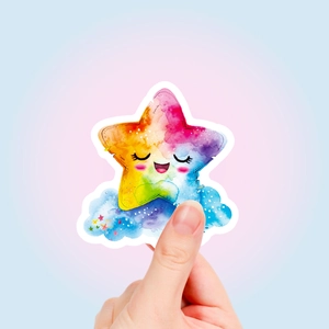Close-up of a colorful watercolor star and cloud sticker held between fingers