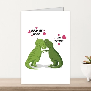 Detail van een wenskaart met twee groene dinosaurussen en hartjes op een plank