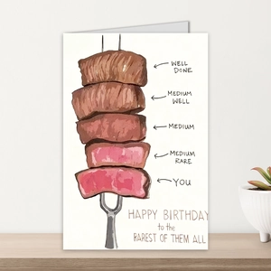Close-up of humorous steak watercolor birthday card on a minimalist wood surface