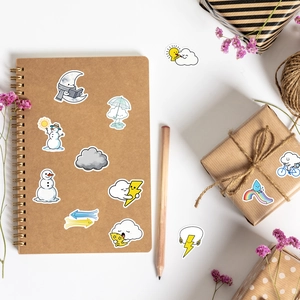 Flat lay of cute weather stickers with sun and clouds on a kraft notebook and gift box