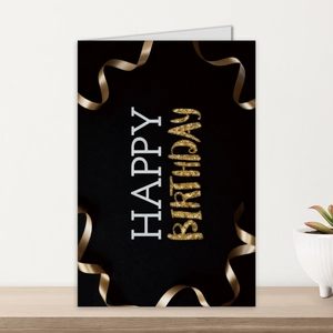 Detail of elegant black and gold Happy Birthday card standing on a wooden desk with a plant