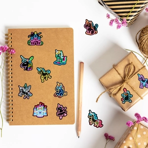 Neon unicorn stickers shown on a kraft paper notebook and gift box with floral decor