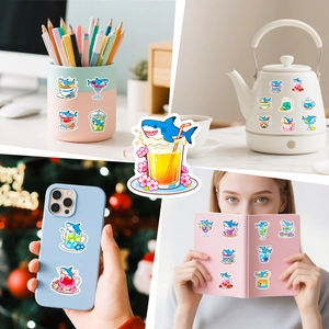 Cute cartoon shark drink stickers shown decorating a notebook, phone case, and kettle