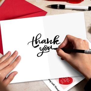 Detail shot of hands writing on a minimalist white thank you card with a red envelope