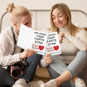 Detail of humorous greeting cards with red hearts held by two women in a cozy home setting