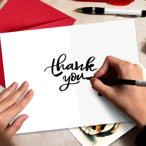 Close-up of red envelope and white thank you greeting card with black calligraphy pen