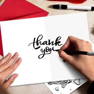Détail de mains écrivant sur une carte de remerciement avec enveloppe rouge et stylos