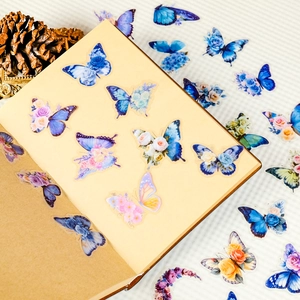 Macro detail of blue butterfly and floral PET stickers on a vintage notebook layout