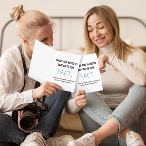 Two women looking at minimalist birthday greeting cards for father on wooden floor