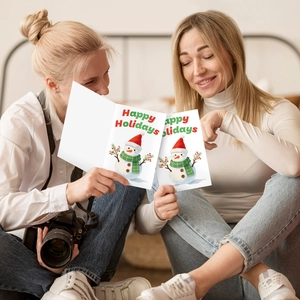 Mujeres compartiendo tarjetas de felicitación navideñas con ilustración de muñeco de nieve