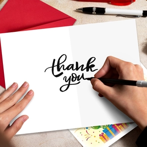 Close-up of a red envelope and a handwritten thank you card with a black pen on a table