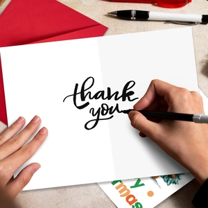 Close-up of handwriting thank you on a white card with a red envelope and pen