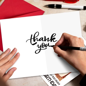 Close-up of birthday and thank you greeting cards with a red envelope and pens on desk