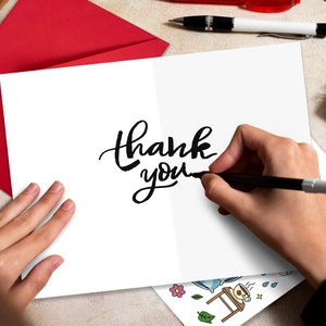 Detail of hand writing on a white 'thank you' card with a red envelope and pen set