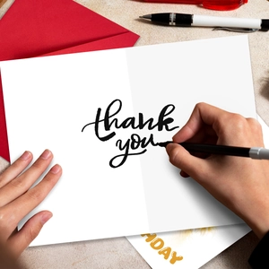 Close-up of minimalist thank you card with red envelope and handwriting on stone surface