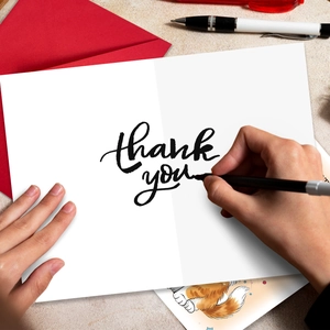 Close-up of white thank you card with elegant black script and a red envelope set