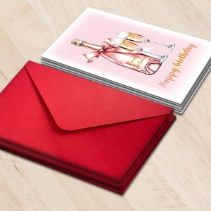 Detail of stacked Happy Birthday cards with champagne art and red envelopes on wood