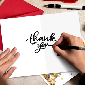 Close-up of a white folding thank you card with red envelope and handwritten calligraphy