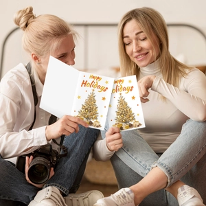 Close-up of friends exchanging elegant gold foil Christmas cards with holiday trees