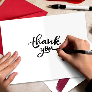 Close-up of handwriting 'thank you' on white matte card with red envelope and pen