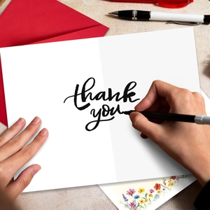 Top view of hand writing on floral thank you card with red envelope and stationery