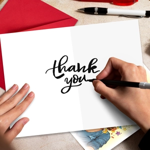 Detailed view of white thank you card with red envelope and pen on desktop