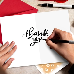 Person writing on a minimalist white thank you card with an elegant red envelope