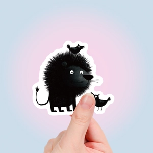 Gros plan d'un autocollant lion noir mignon avec bordure blanche tenu entre les doigts