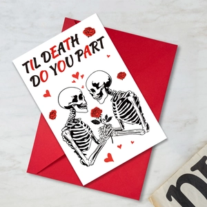 Detalle macro de tarjeta de San Valentín gótica con calaveras y sobre rojo en mármol