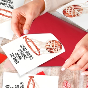 Detail showing a hand placing a basketball-themed watercolor greeting card into a red envelope