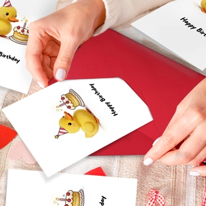 Placing a cute yellow duck birthday card into a vibrant red envelope by hand