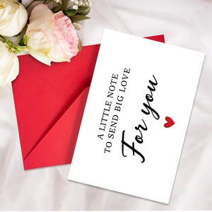 Close-up of a white note card with big love text and a matching red envelope on silk fabric