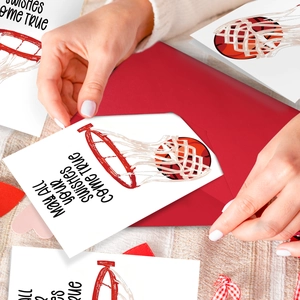 Hand inserting basketball wish card into red envelope on a cozy rustic fabric background