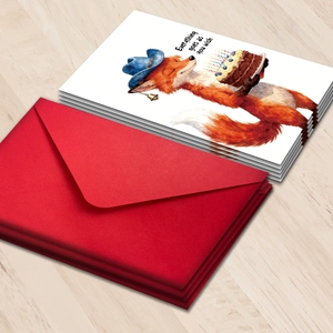 Cartoon fox with cake birthday card set and red envelope on a light wood background