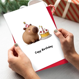 Capybara Cartoon Geburtstagskarte mit rotem Umschlag auf einem festlichen Geschenktisch