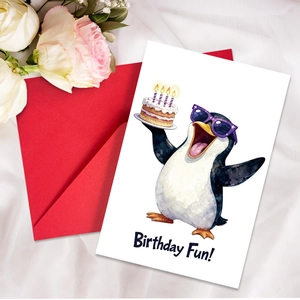 Close-up of watercolor penguin birthday card with red envelope on white silk cloth