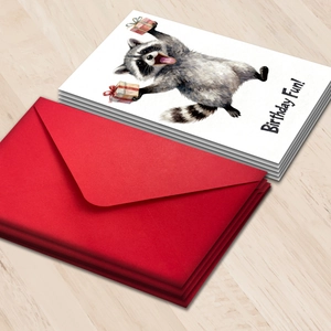 Birthday card with watercolor raccoon and red envelope on light wood background