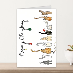 Dettaglio biglietto Meowry Christmas con gatti su scrivania in legno vicino a pianta bianca