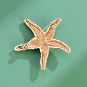 Golden starfish brooch showing the back structure with needle clasp on green background