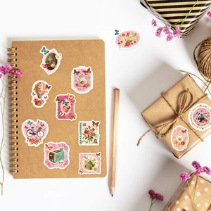 Dettagli di adesivi floreali vintage rosa su un taccuino e una confezione regalo