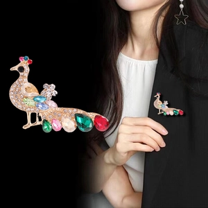 Broche paon élégante avec strass colorés sur base dorée, portée sur blazer noir