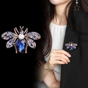 Luxurious bee brooch with blue crystal and pearls shown on a black suit jacket
