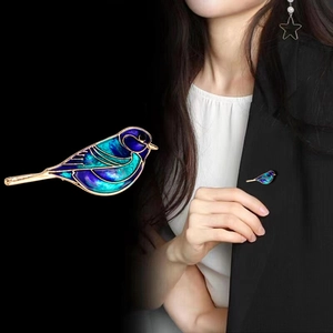 Detail van een vogelbroche met blauw email en gouden lijnen op een donker colbert
