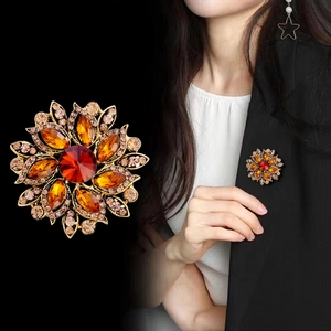 Vintage gold flower brooch with amber rhinestones and a central red crystal on black blazer
