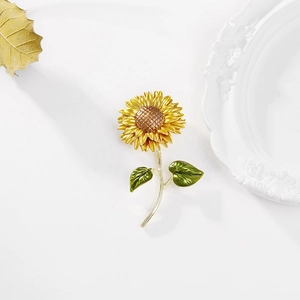 Detailed view of yellow enamel sunflower brooch with textured petals on a white surface