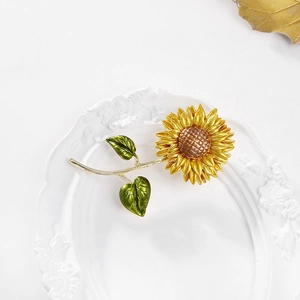 Creative sunflower enamel brooch with yellow petals and green leaves on a white tray