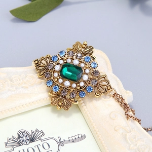 Broche baroque émeraude avec perles et chaîne dorée sur cadre vintage beige