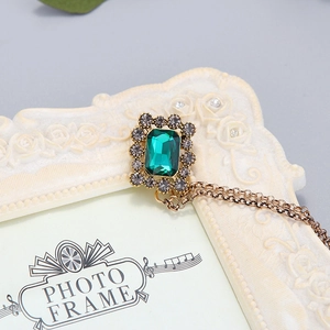 Détail d'une broche baroque avec pierre verte taille émeraude et chaîne dorée rétro