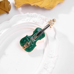 Close-up of green enamel violin brooch with gold accents on a white decorative tray