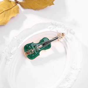 Elegant gold and emerald enamel violin brooch displayed on a white embossed tray